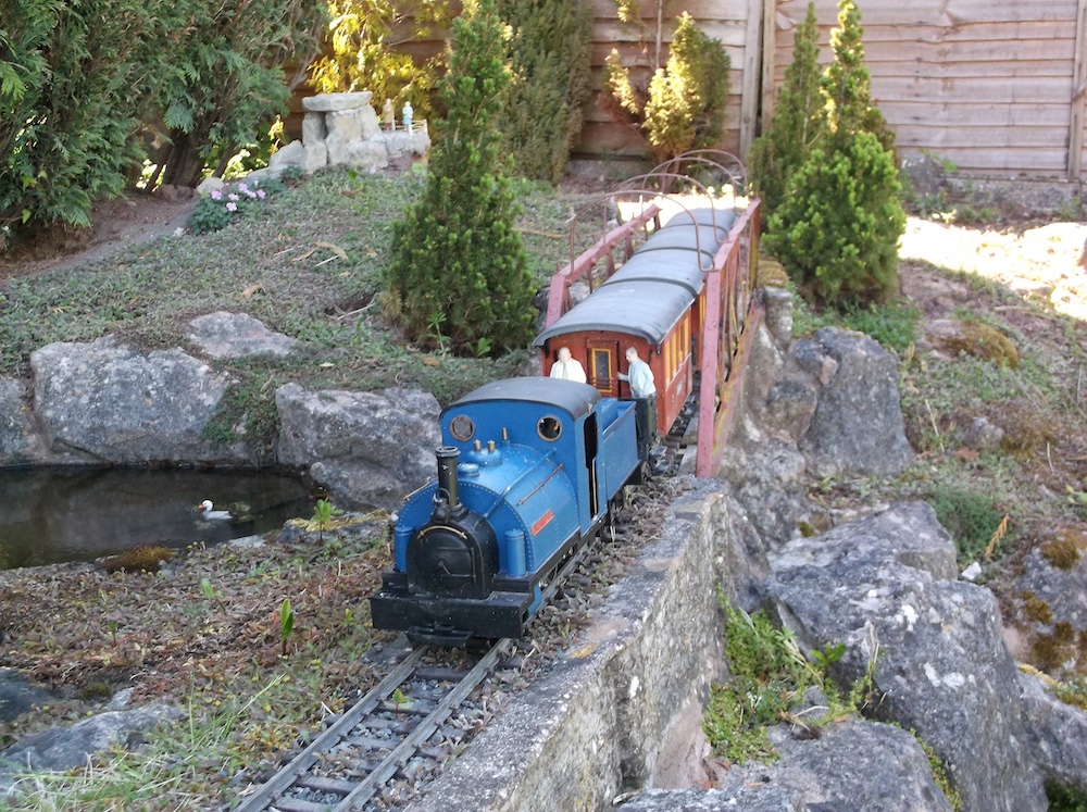 blue steam locomotive with passenger cars on garden railway