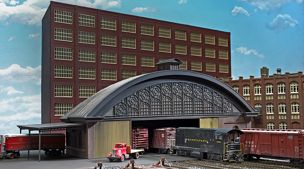 A model railroad structure with a blue sky background and trains protruding from the structure on the base level