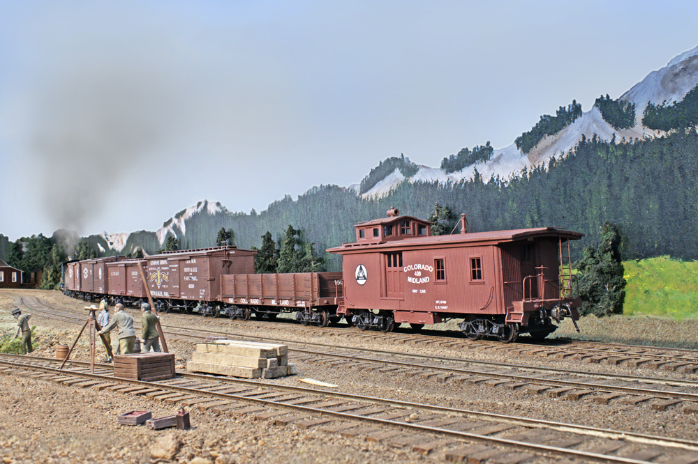 Color photo of model train passing through a mountain scene.