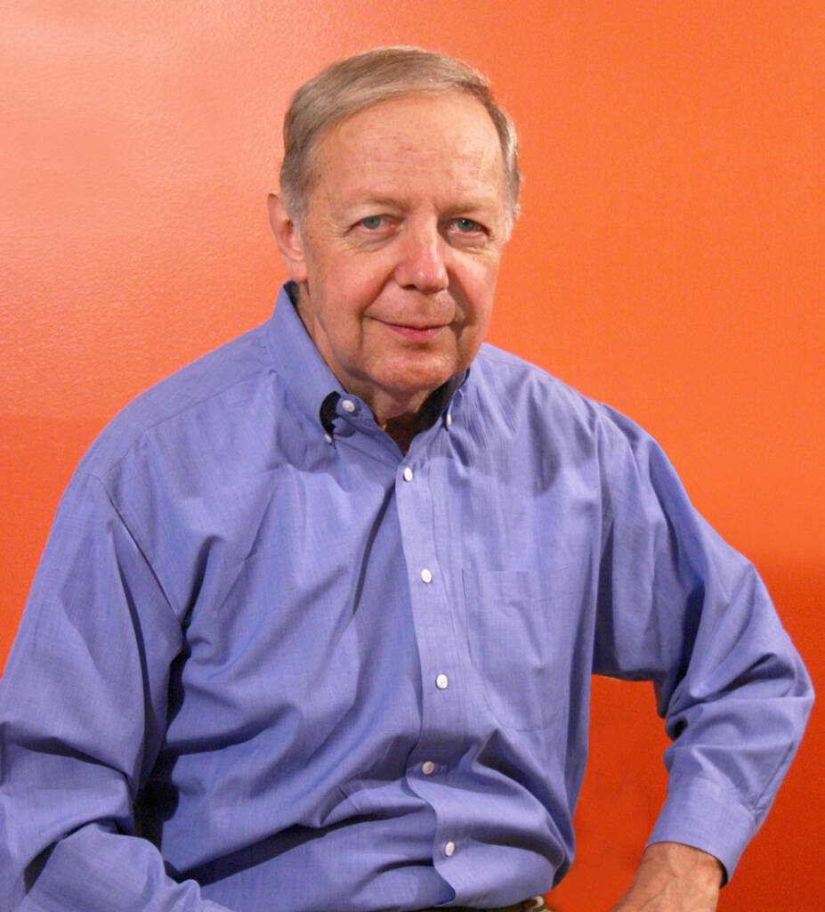 Color photo of man in blue shirt in front of orange background.