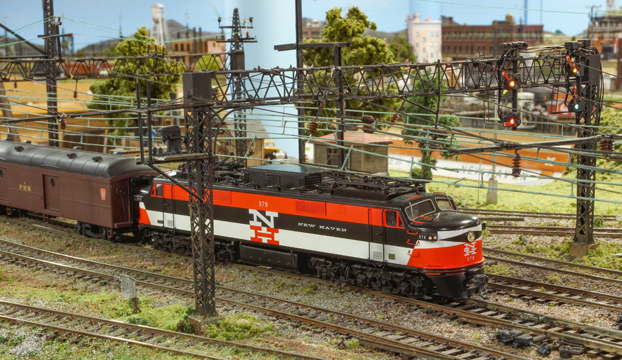 Orange, black, and white model electric locomotive running under catenary.