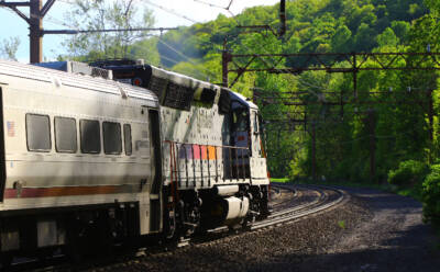 Silver diesel locomotive pulling a passenger train. 