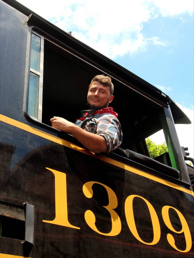 Young individual leaning out of the cab of a steam locomotive.