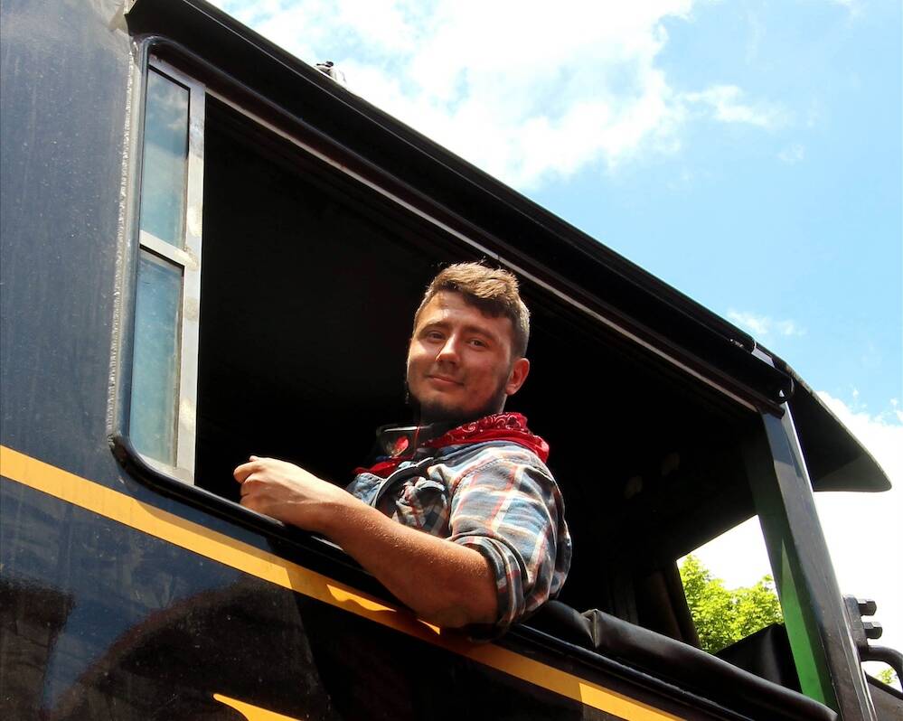 Young individual leaning out of the cab of a steam locomotive.