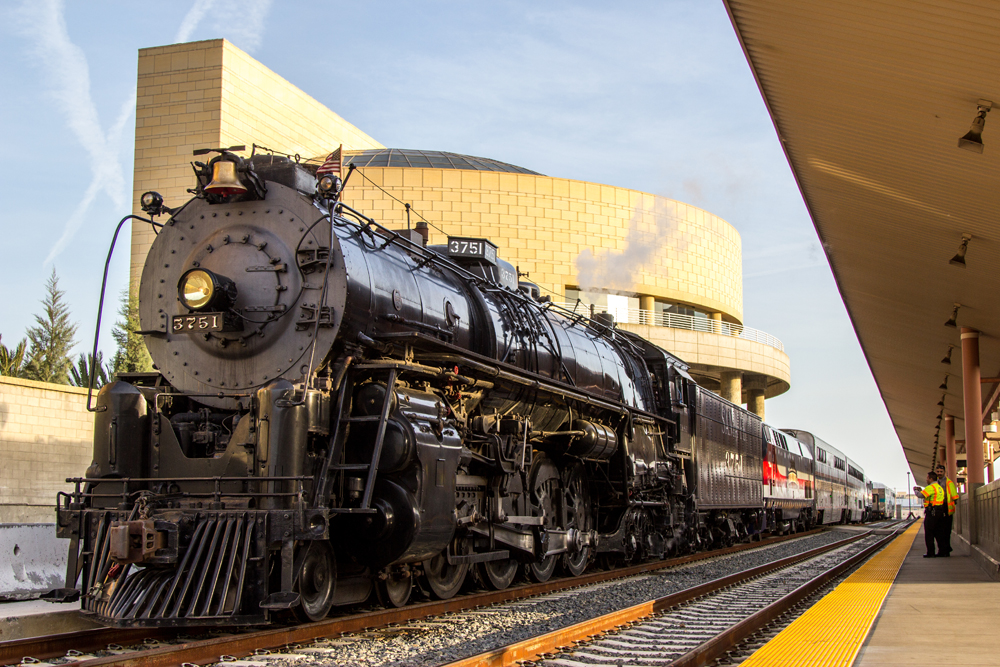 Steam locomotive at passenger station with modern building in background