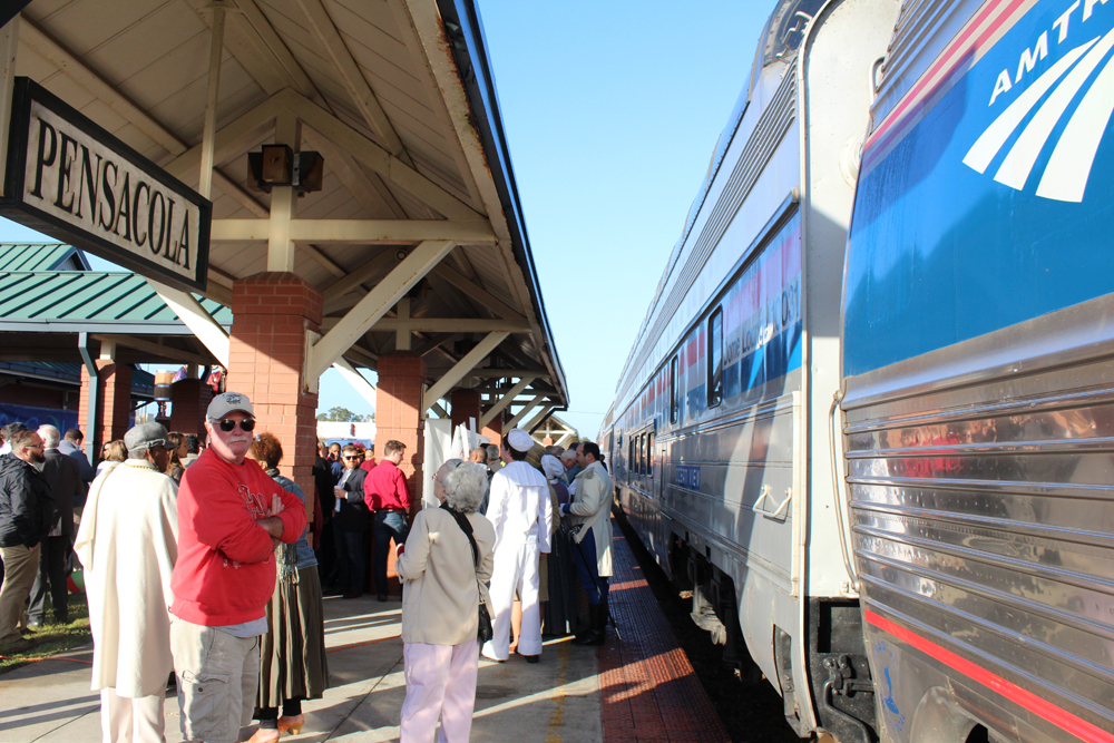 Train at station with "Pensacola" sign visible on platform roof. 