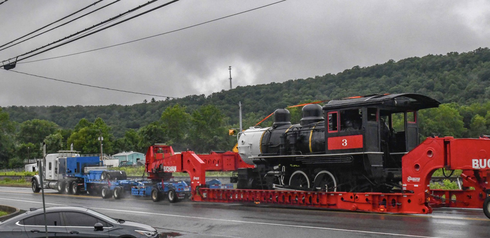 Steam locomotive moving on highway on goose-neck truck trailer.