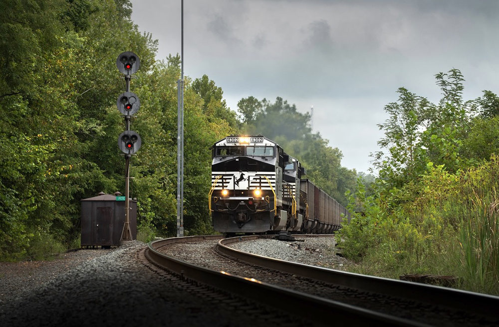 Black and white locomotives with coal hoppers cresting hill