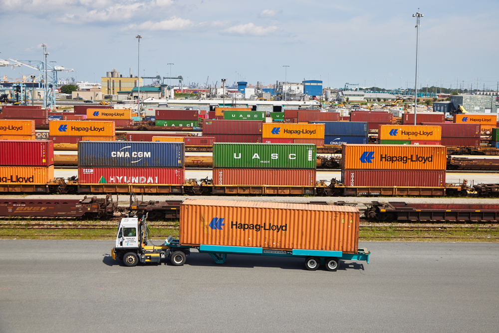 Truck with container in front of several tracks of container railcars at port