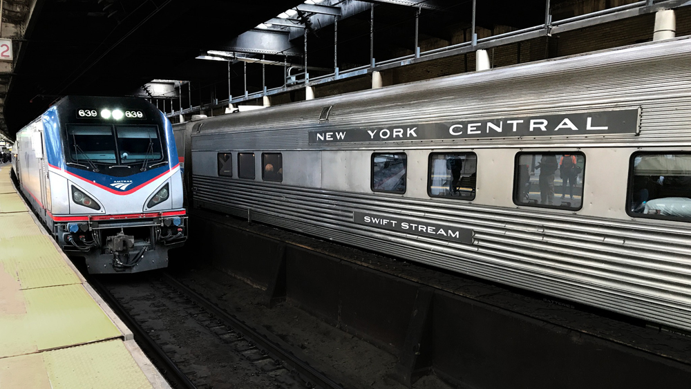 Stainless steel passenger car next to electric locomotive in station