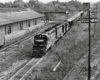 Three black diesel Atlanta & West Point locomotives with freight train by building with loading dock