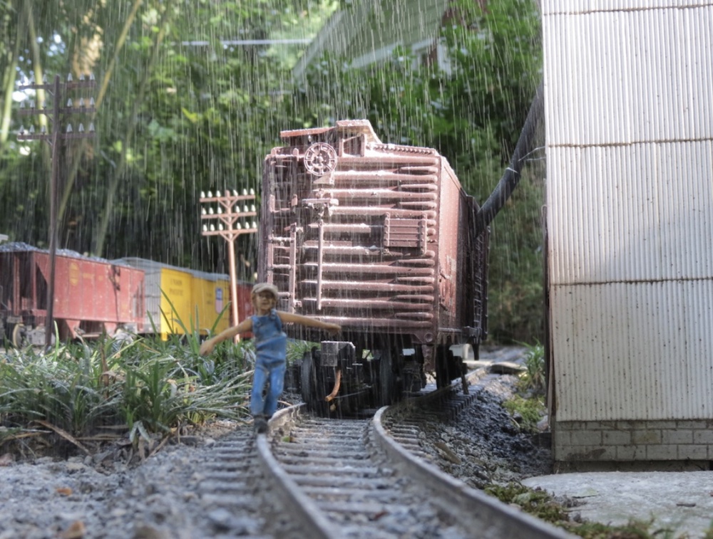 a figure of a child walks on the rails next to a boxcar on garden railway