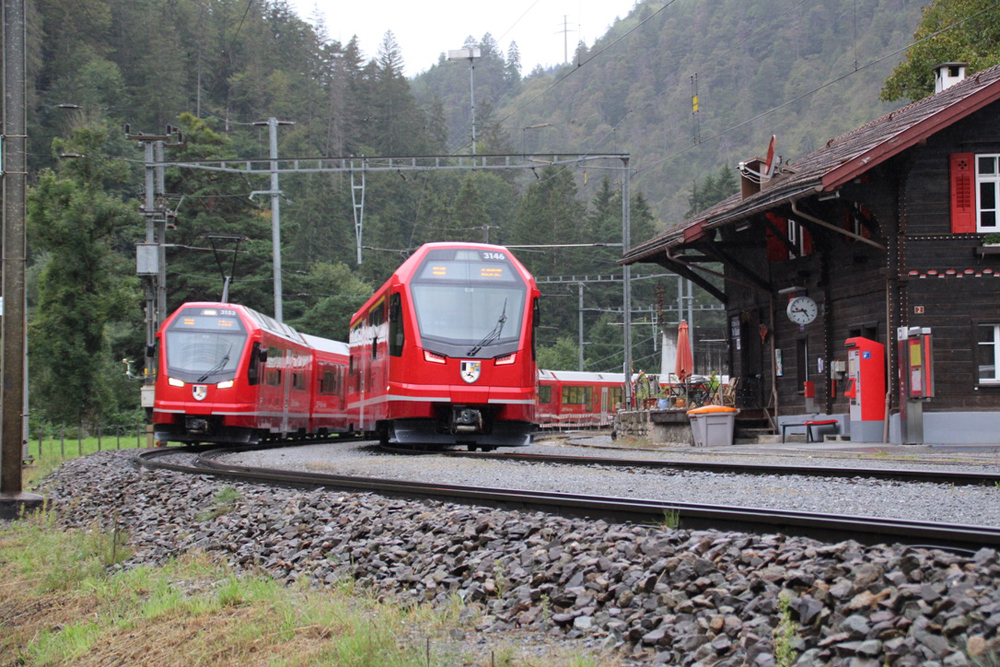 Two red EMU trains meet at station in mountains