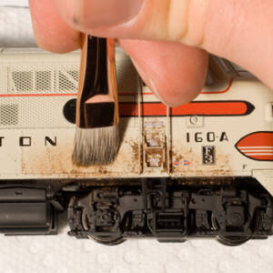 A brush applies rust-red powder to a white model locomotive