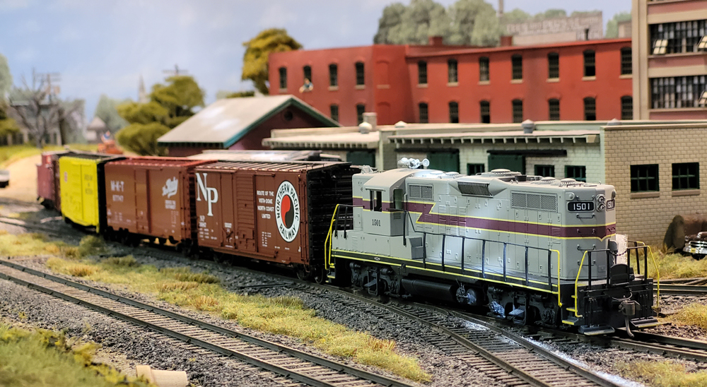 A model train on a model train layout is led by a gray locomotive