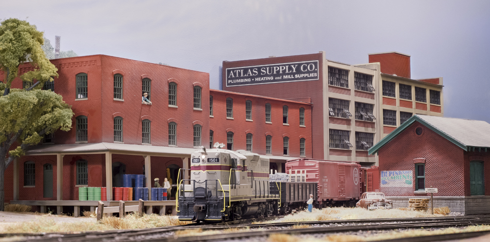 Color photo HO scale train with assorted brick buildings in background.