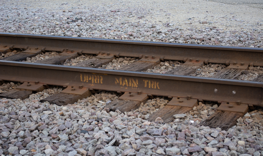 Color photo of railroad track with yellow stencil applied to web of the rail.