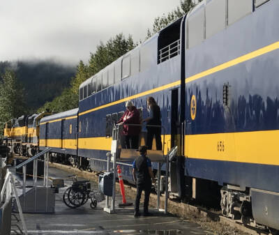 Passenger and trainman on ADA lift next to blue and yellow passenger train.