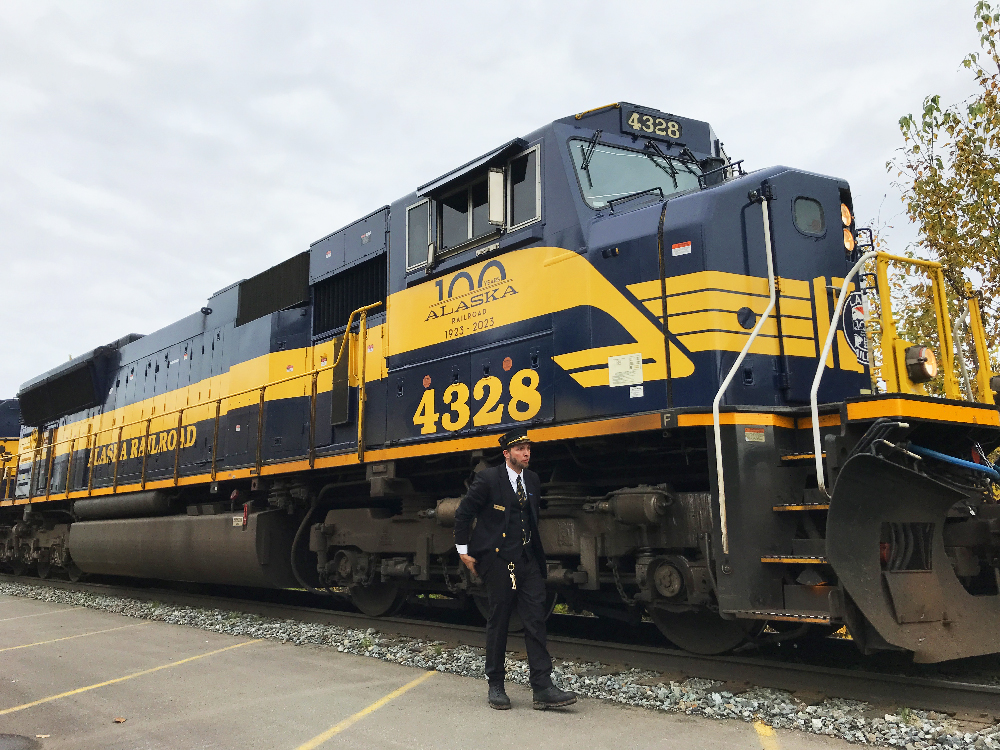 Conductor next to blue and yellow diesel locomotive. Alaska by rail journey.