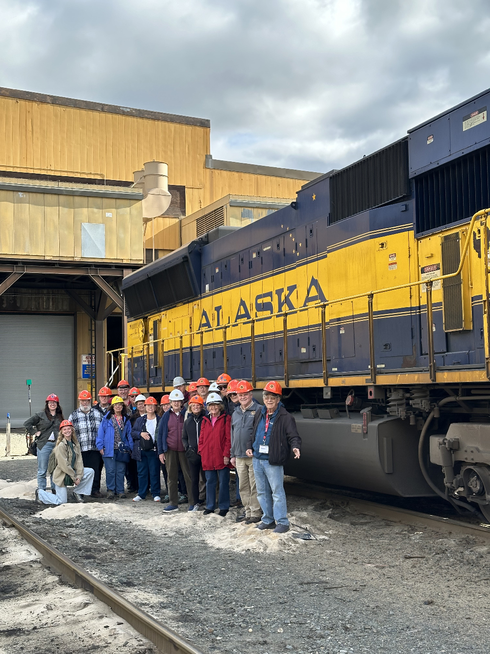 Group standing by blue and yellow diesel locomotive.