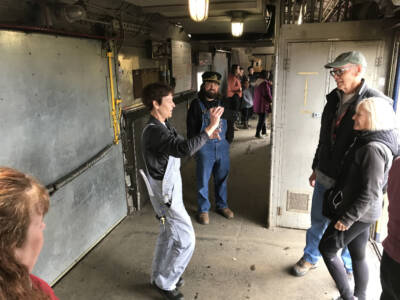 Lady taking a photograph of a couple standing in a baggage car.