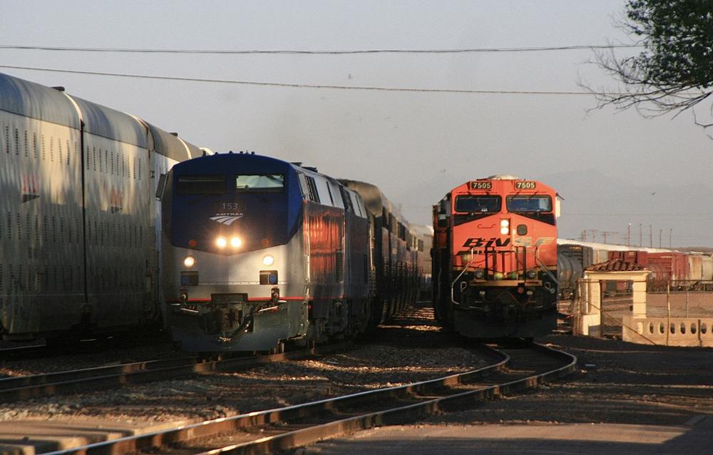 Passenger train passes freight with orange locomotive