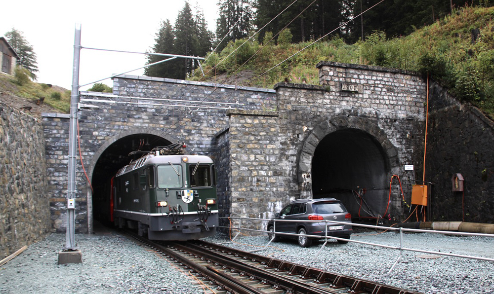 Green electric locomotive emerging from tunnel.