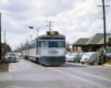 Electric interurban car in stainless-and-blue on street trackage