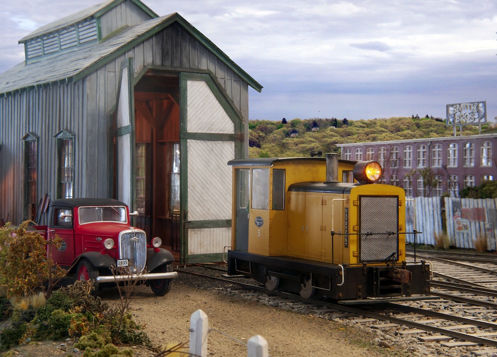 yellow switcher engine next to enginehouse with red truck nearby