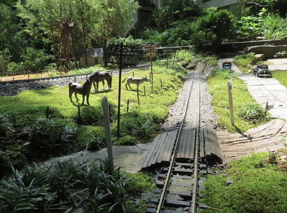 grade crossing on garden railway with horses nearby; Capturing reality in garden railway photographs