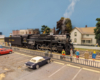 A black model steam locomotive in a town setting on a model railroad layout