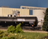 A model figure clad in orange stands next to a black model tank car