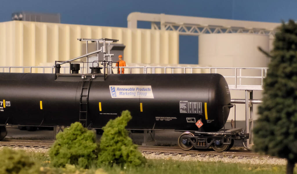 Milwaukee Racine & Troy retrospective gallery: A man clad in orange high visibility gear stands next to a model tank car on a model railroad layout