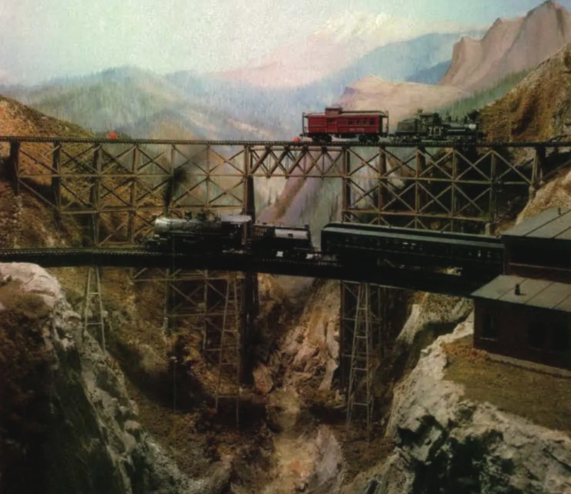 Model steam train on a trestle in front of a painted background