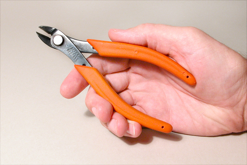 Color photo of hand holding cutting tool with orange handles.