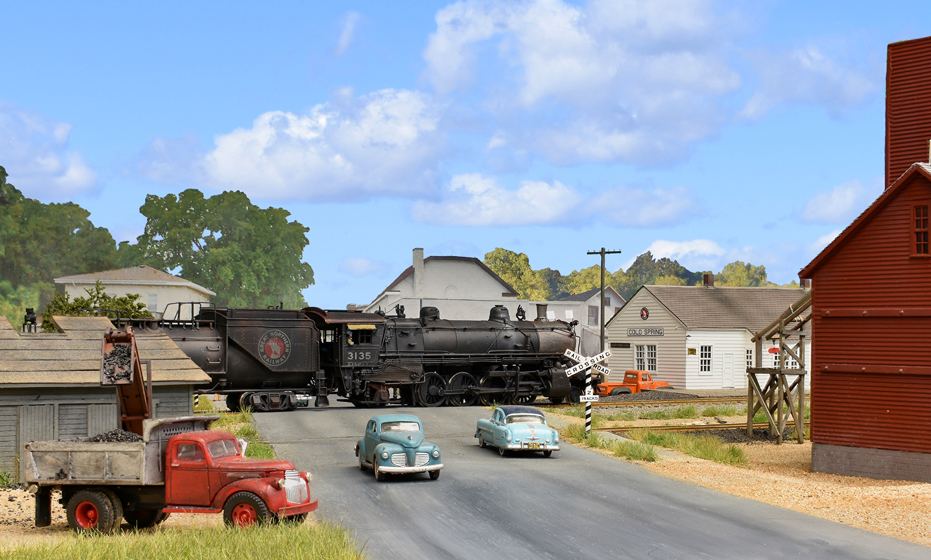 Color photo of steam locomotive passing through a small town.