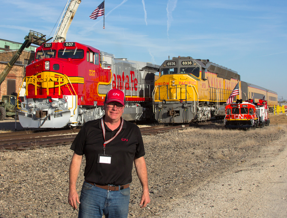 Man in black shirt with Santa Fe and Union Pacific locomotives in background