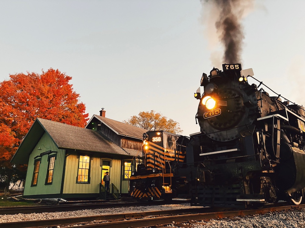 Steam and diesel locomotives next to a wooden depot