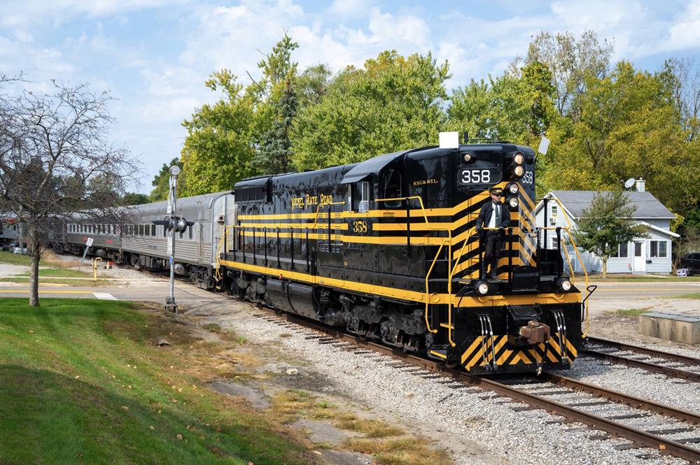 Black diesel with yellow stripes pulling passenger train