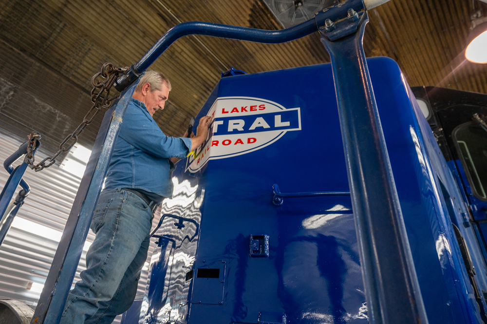 Man working on logo on nose of blue locomotive