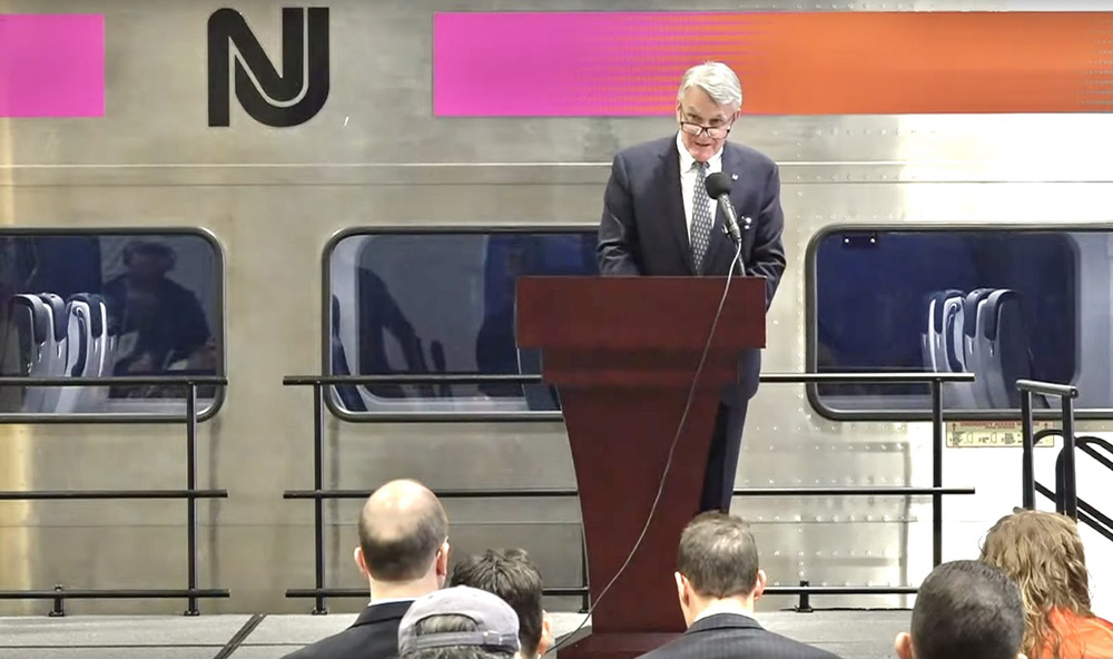 Man at podium with railcar in background