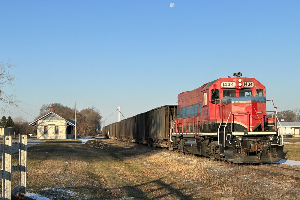 Red locomotive with green stripe with train of ballast cars