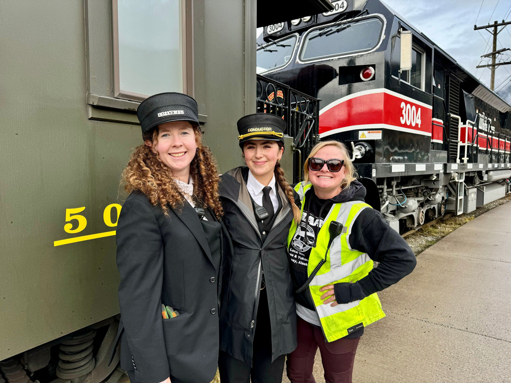 Three women posed next to passenger car and diesel locomotive