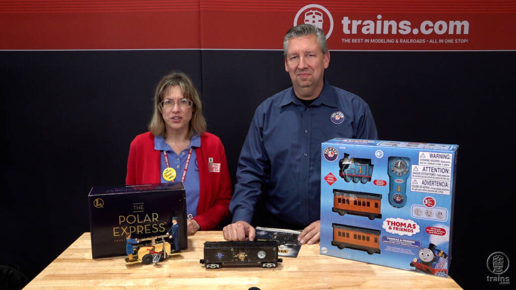 woman and man standing behind table with toy train items on the table