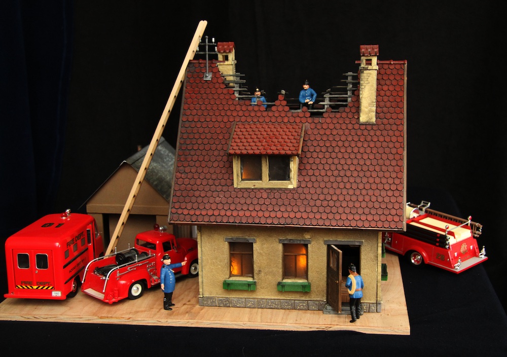 model of burning house with fire truck and vehicles around it