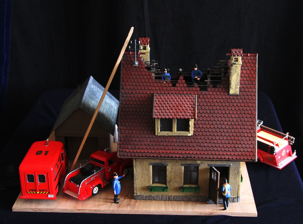 model of burning house with fire truck and vehicles around it