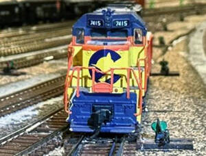 A yellow and blue Chessie System EMD diesel locomotive sits next to a switch stand facing the camera in an N scale yard