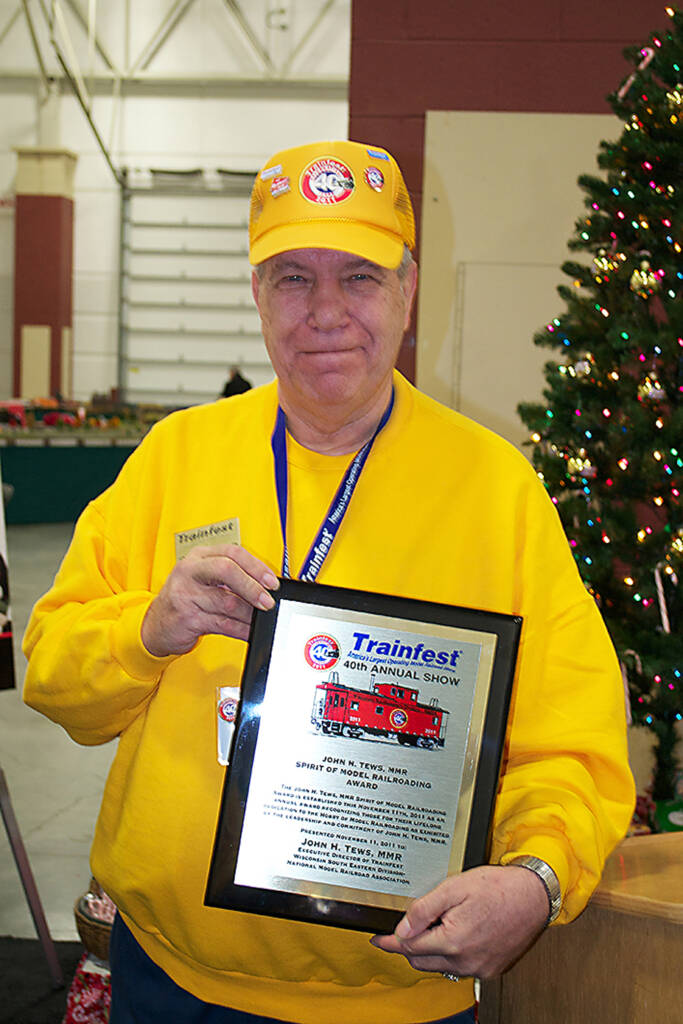 Color photo of man in yellow hat and shirt with award.