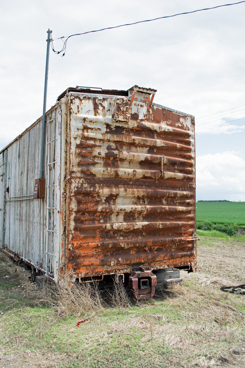 Color image showing end of boxcar with peeling white paint and rust.