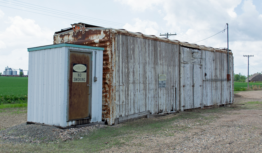 Color photo of small metal shed next to weathered 40-foot boxcar.